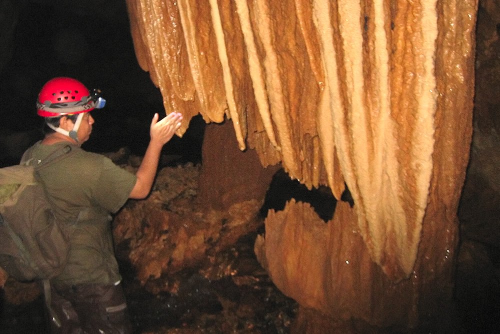 A person wearing a red helmet follows the light of their headlamp to explore rock formations.