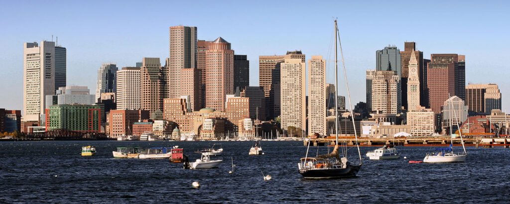 A panoramic view of the Charleston harbor with boats floating on the water and a city skyline in the background.