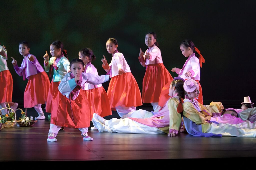 A group of children in colorful traditional costumes perform on stage.