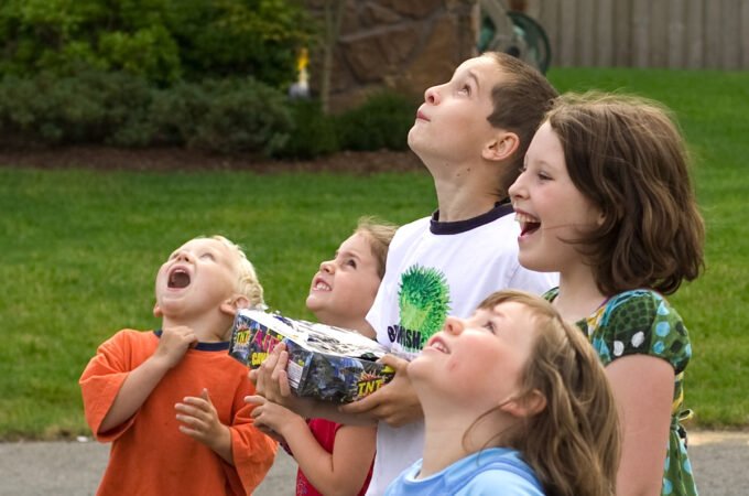 A group of children outdoors, smiling and looking up in excitement. They appear to be part of a joyful celebration.