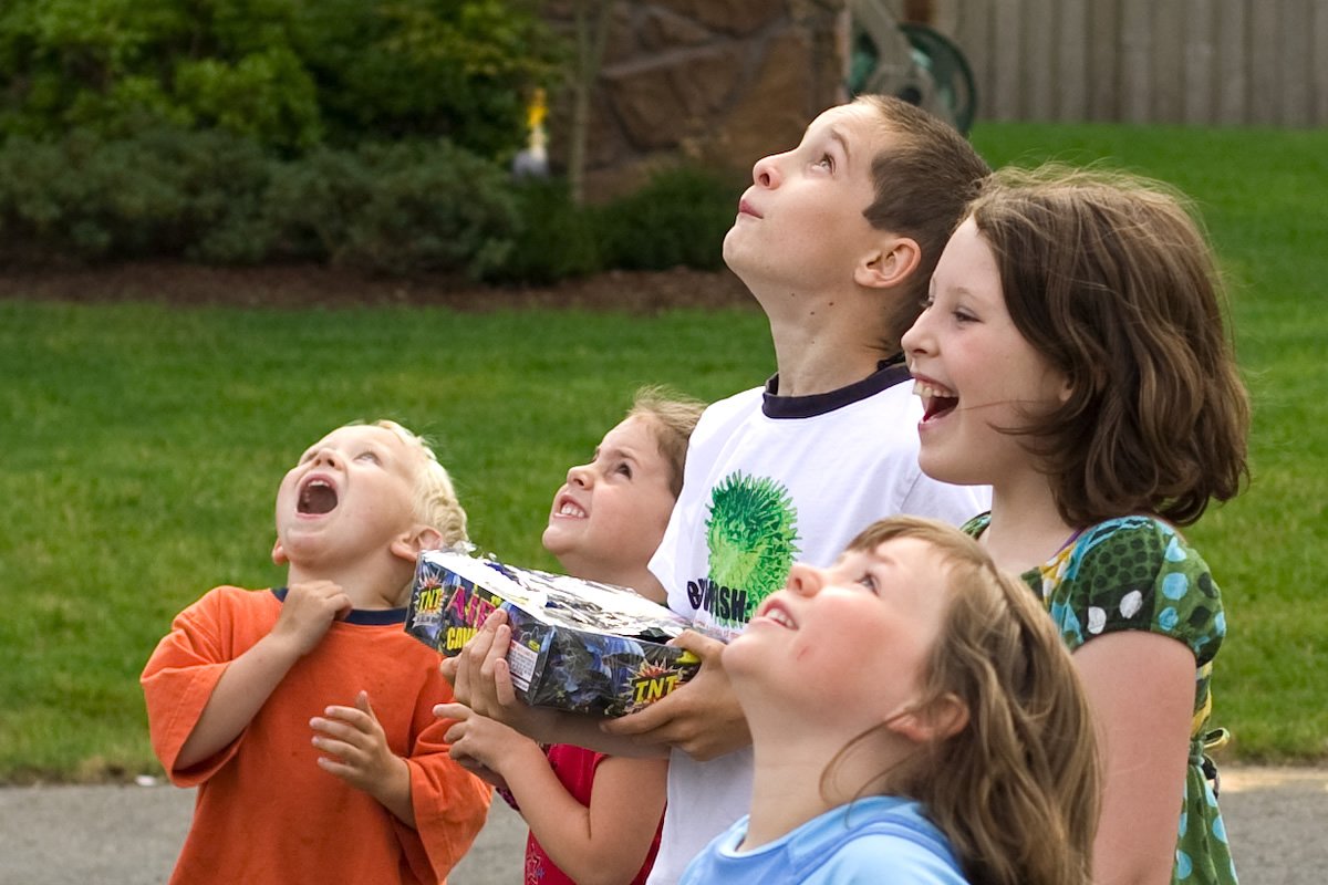 Fourth of July A group of children outdoors, smiling and looking up in excitement. They appear to be part of a joyful celebration.
