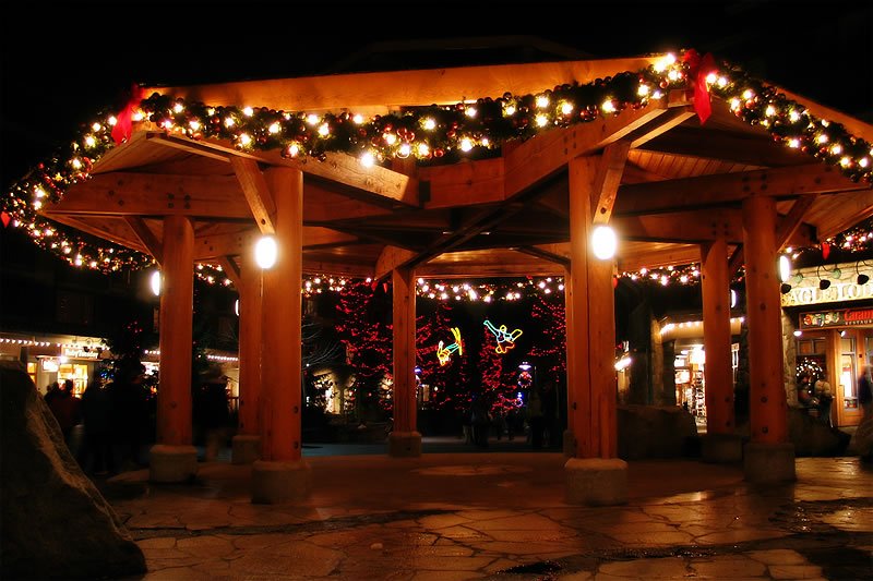 A beautifully decorated pavilion adorned with twinkling Christmas lights and garlands under the night sky. Warm lights illuminate the wooden structure, creating a cozy and inviting atmosphere.