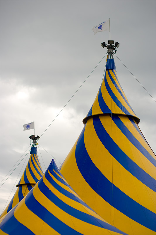 Circus tents with blue and yellow stripes under a cloudy sky.