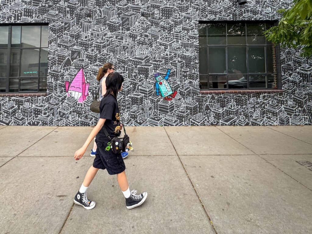 A person walking by a colorful mural with vibrant sailboats and urban sketches.