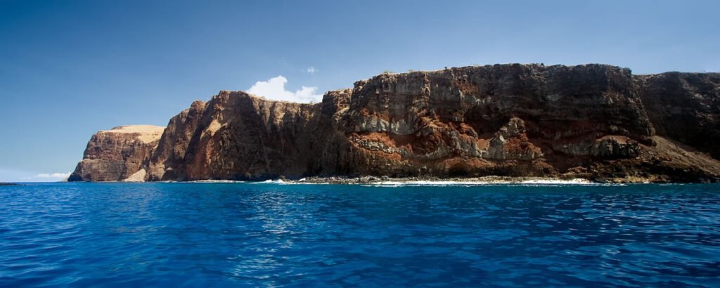A breathtaking view of rugged cliffs rising sharply from the deep blue ocean under a clear sky.