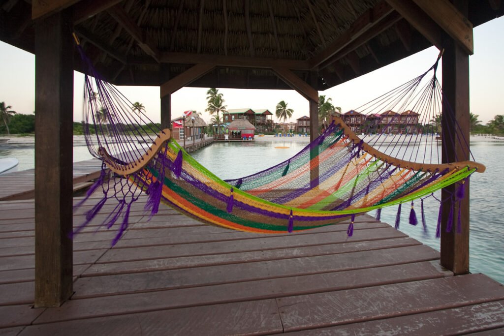 A vibrant hammock hangs under a wooden pavilion by a serene lake.