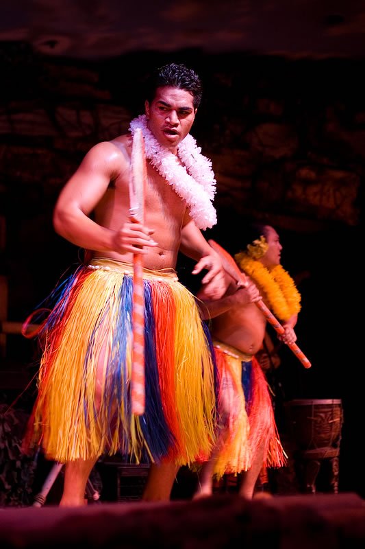 Two dancers in vibrant, multicolored grass skirts performing on stage.