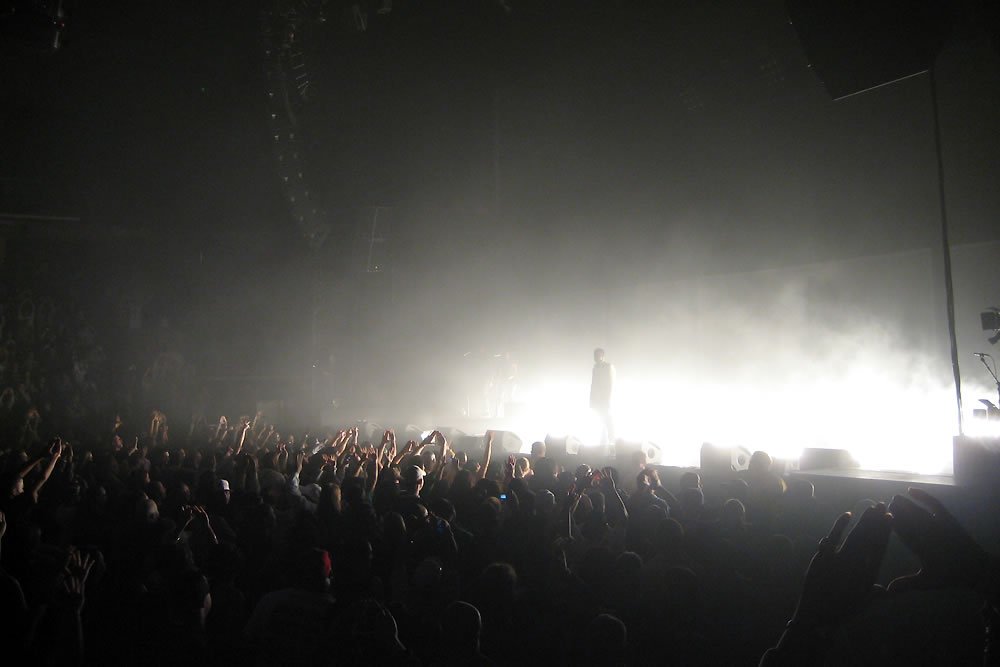 A crowd of people silhouetted against bright stage lights during a concert.