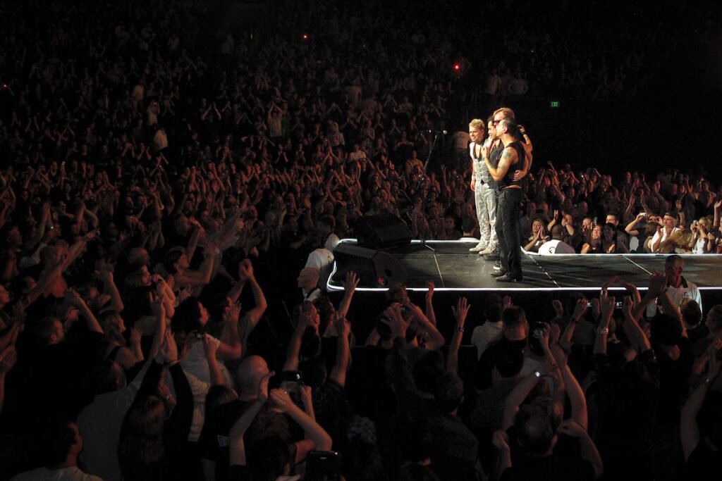 Performers on stage with an enthusiastic crowd cheering in a dimly lit venue.
