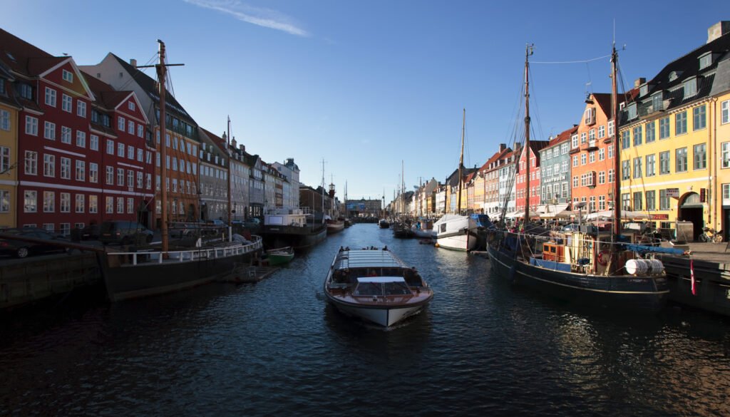 A picturesque canal scene featuring vibrant buildings and moored boats on both sides, under a clear blue sky.