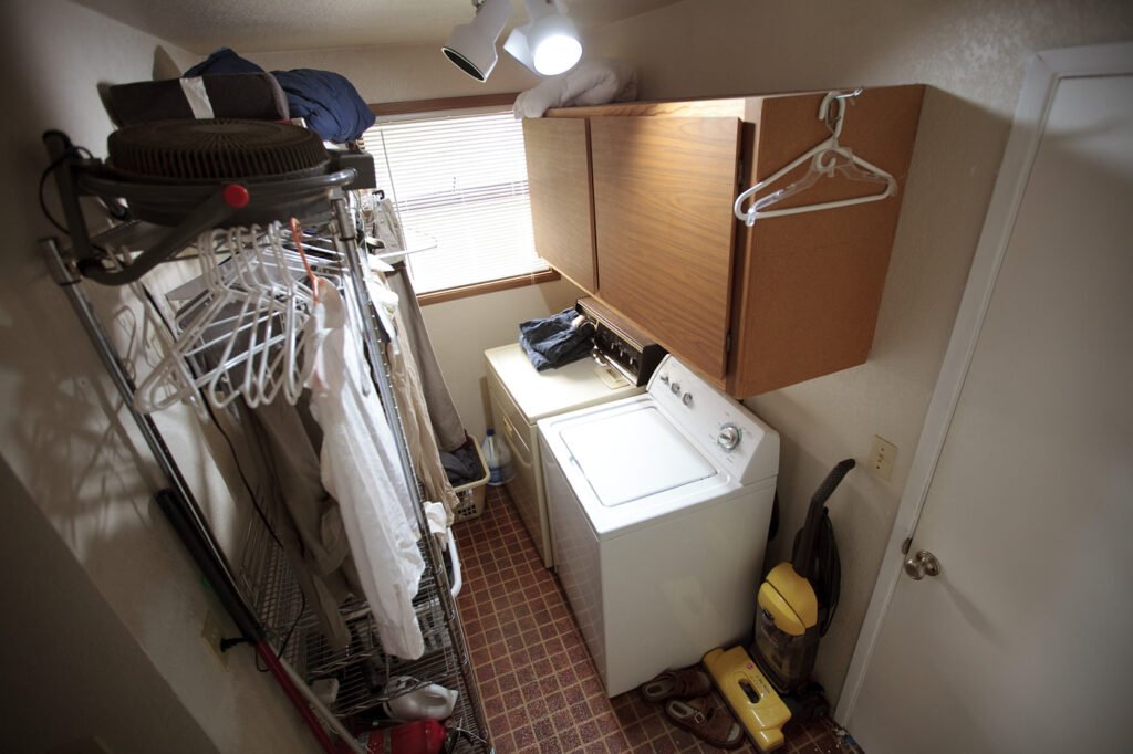 A small, efficient laundry room with a washer and dryer, featuring a vacuum cleaner and neatly hung clothes.