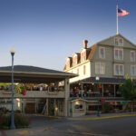 200th Post A charming restaurant with outdoor seating areas, featuring an American flag flying high on a pole. The building has multiple stories with large windows and a welcoming entrance.