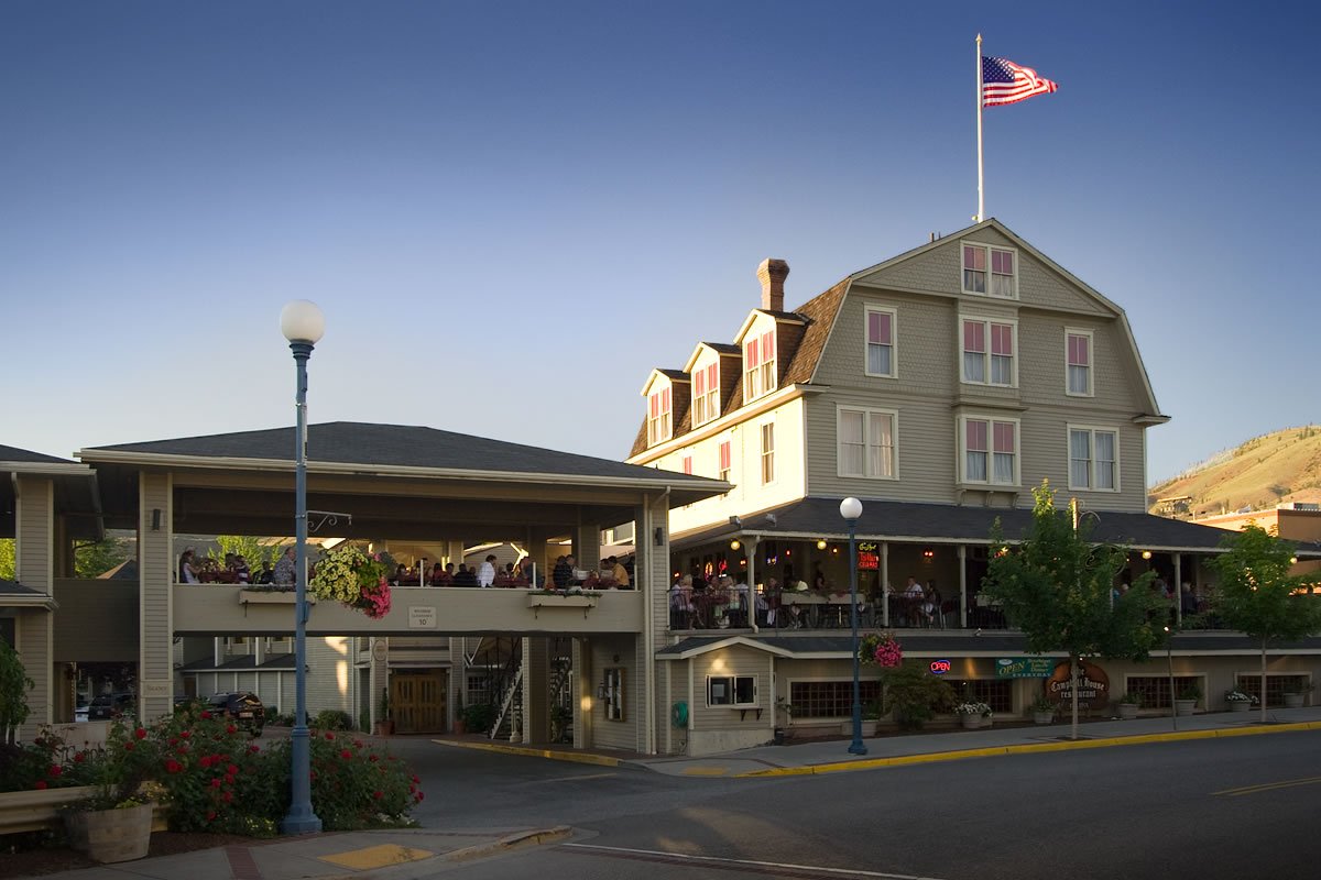 Campbell’s Resort A charming restaurant with outdoor seating areas, featuring an American flag flying high on a pole. The building has multiple stories with large windows and a welcoming entrance.