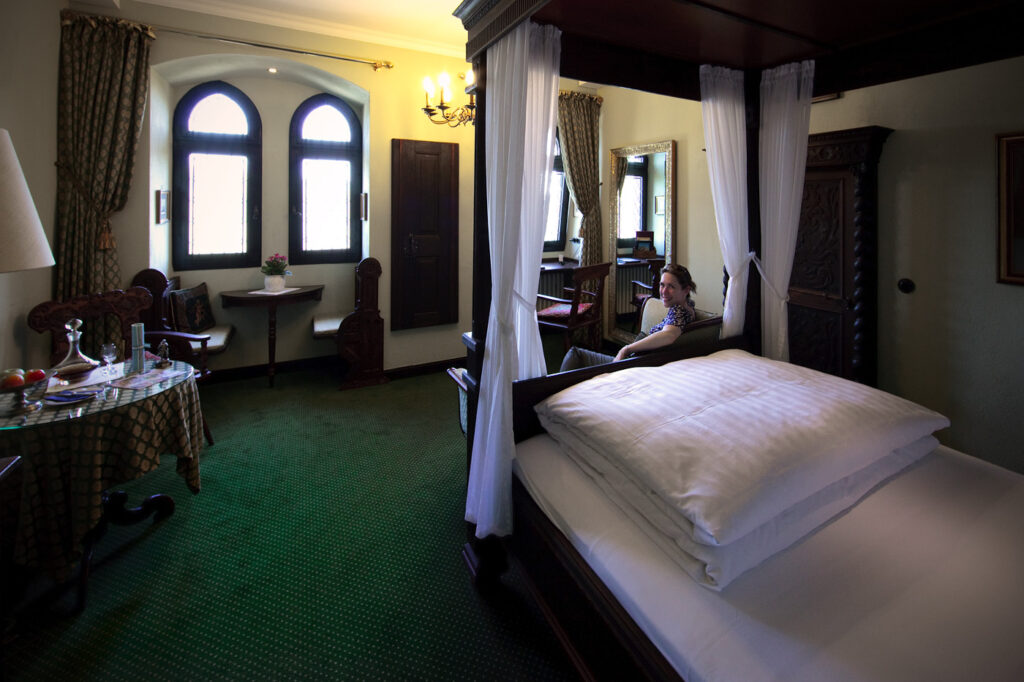 A classic bedroom featuring a four-post bed and arched windows with green carpeting.