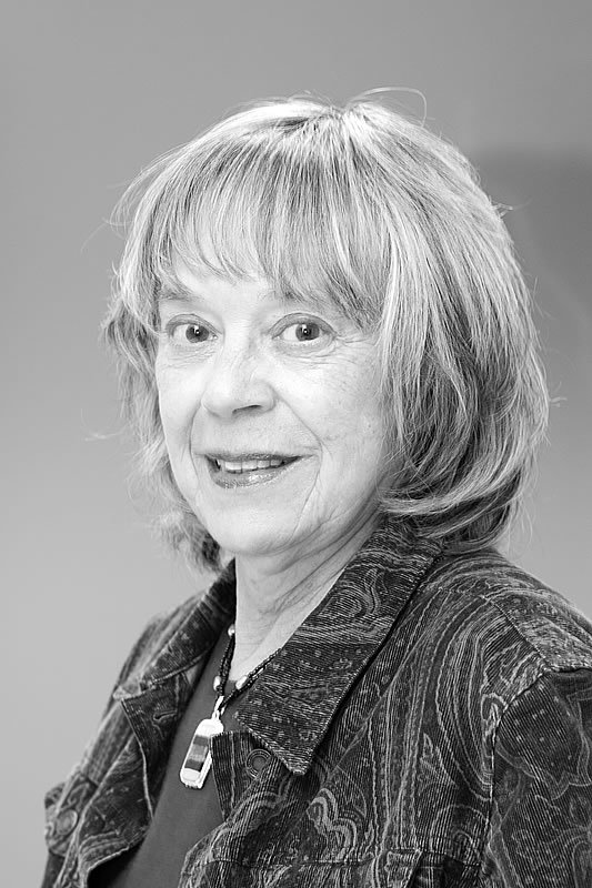 A smiling woman wearing a patterned jacket is captured in a black and white photograph. Her warm expression and cozy demeanor highlight her personality.