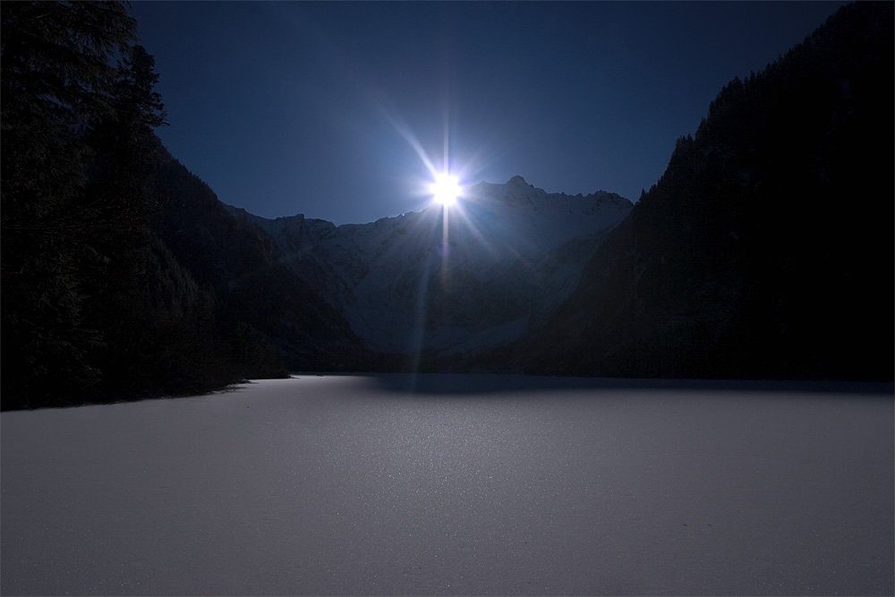 A serene view of Crescent Lake with dense fog and the sun peeking through the mountains.