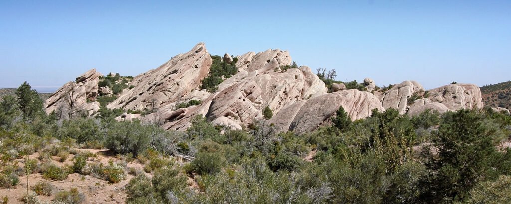 A scenic view of desert landscape with large rock formations and green shrubs under a clear blue sky.