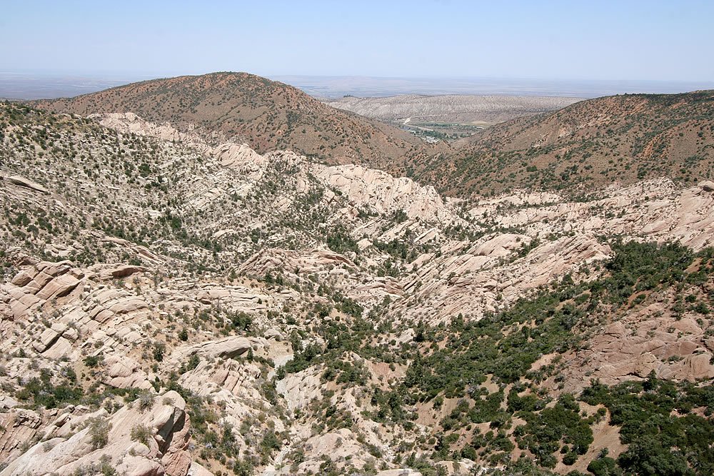 A view of a rugged desert landscape featuring rocky terrain and sparse vegetation under a clear sky.