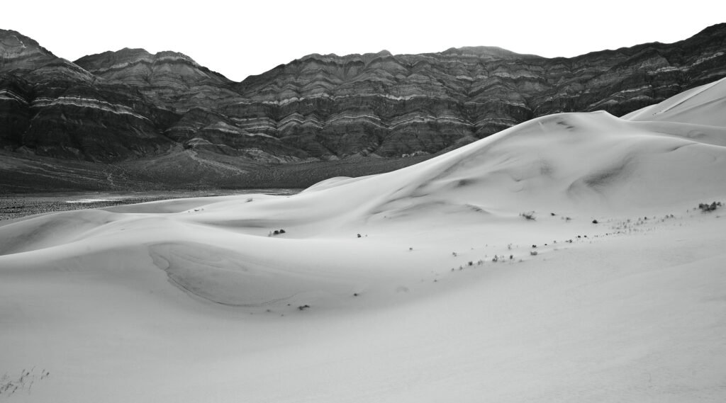 A vast desert landscape with rolling sand dunes in the foreground and rugged, rocky outcrops in the background.
