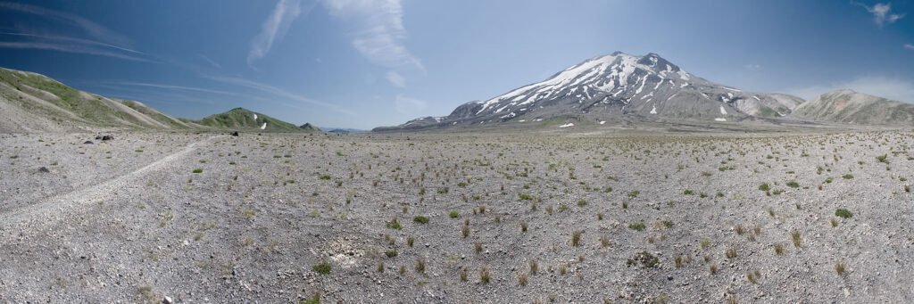 A panoramic view of a barren desert stretching towards snow-capped mountains under a clear blue sky.