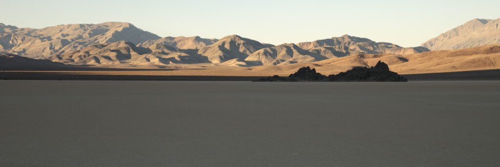 A serene desert landscape with rugged mountains in the background under a soft sunset sky.