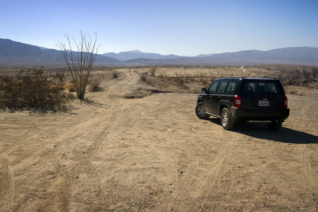 A black SUV parked on a sandy desert trail with mountains in the background.