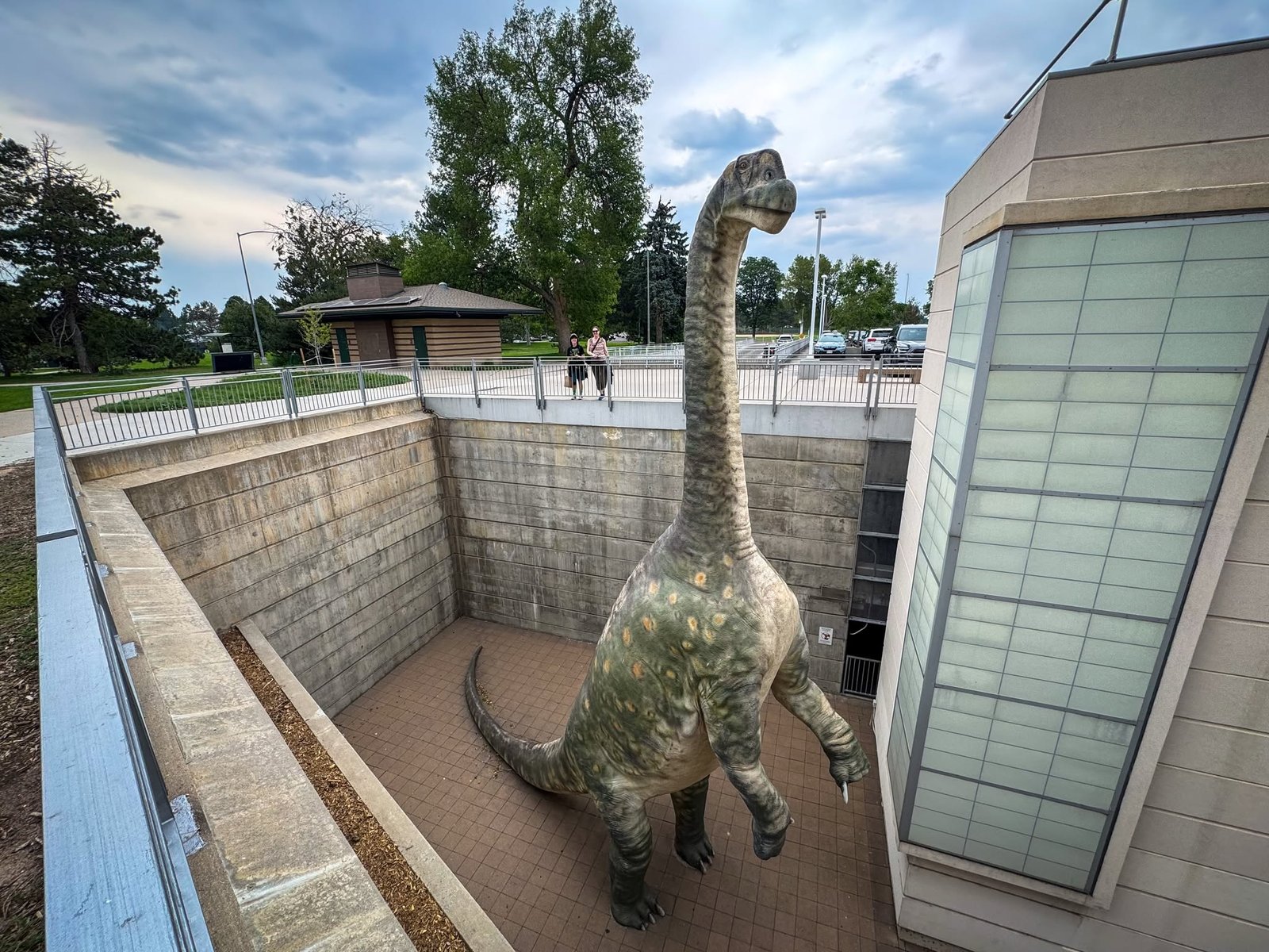 Denver Museum of Nature & Science A large dinosaur illustration stands prominently inside a building, surrounded by windows and modern architectural elements.