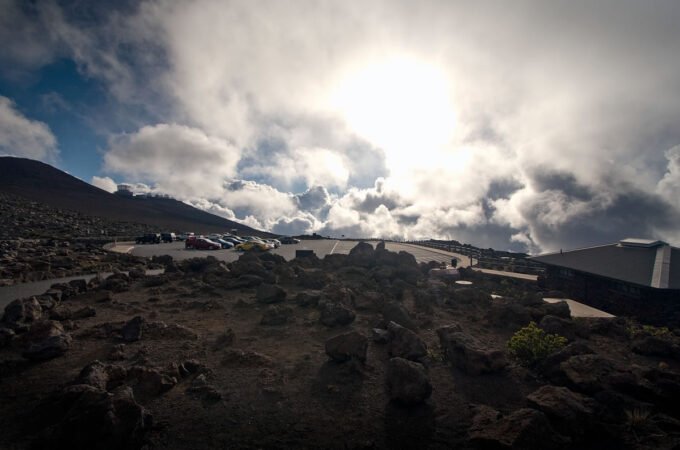 A panoramic view of a dramatic sky with scattered clouds above a rugged landscape of rocks and dirt. The sun shines brightly through the clouds.