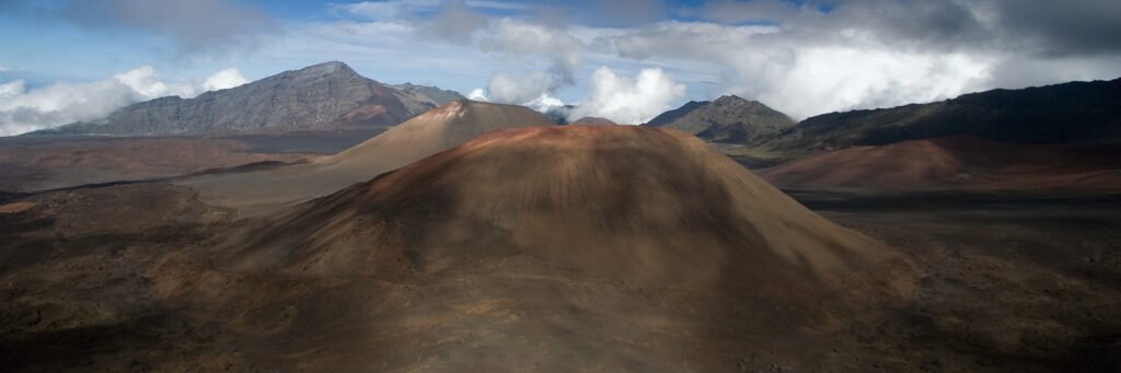A vast mountain range with rugged peaks and rolling hills under a partly cloudy sky.
