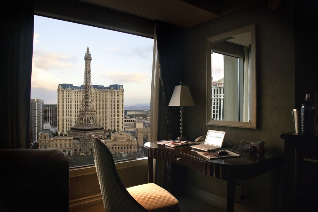 A view of the Eiffel Tower replica in Las Vegas from a hotel room window with a chair and desk inside.