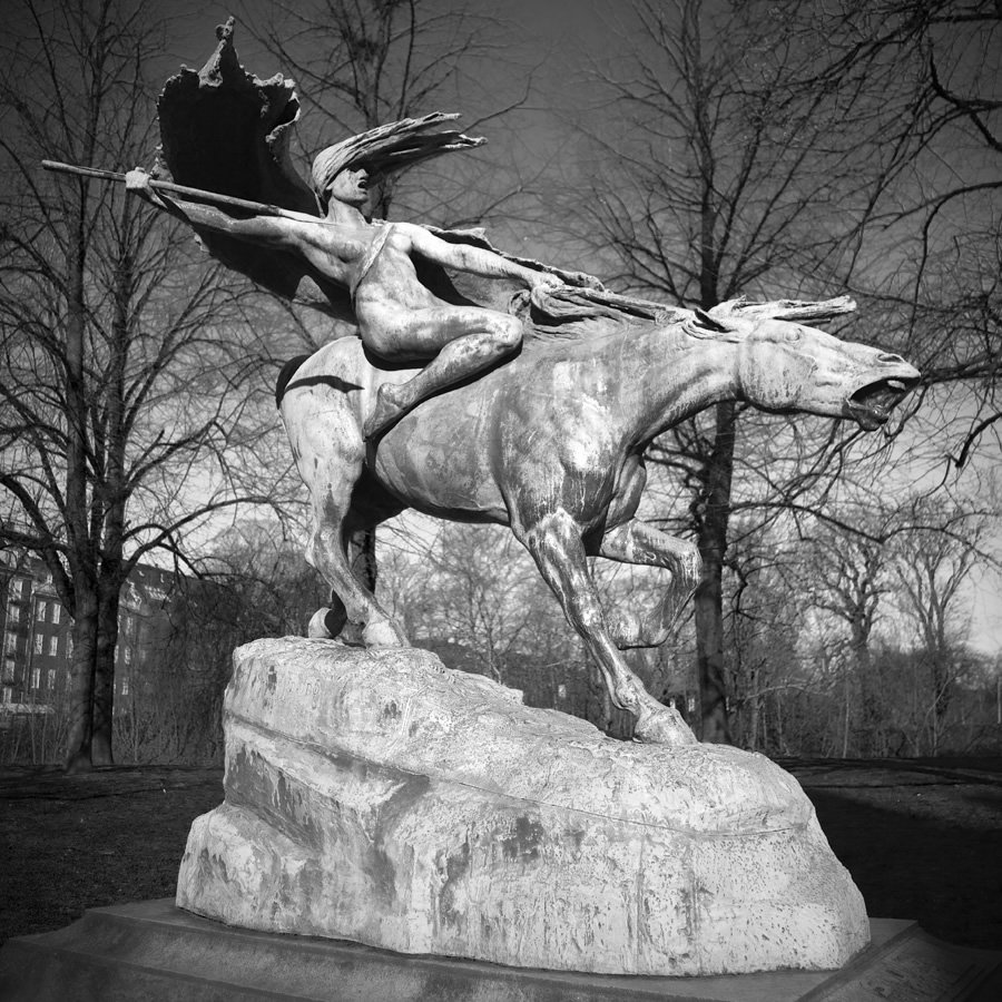 A striking black and white depiction of a powerful equestrian statue with an animated figure wielding a spear.