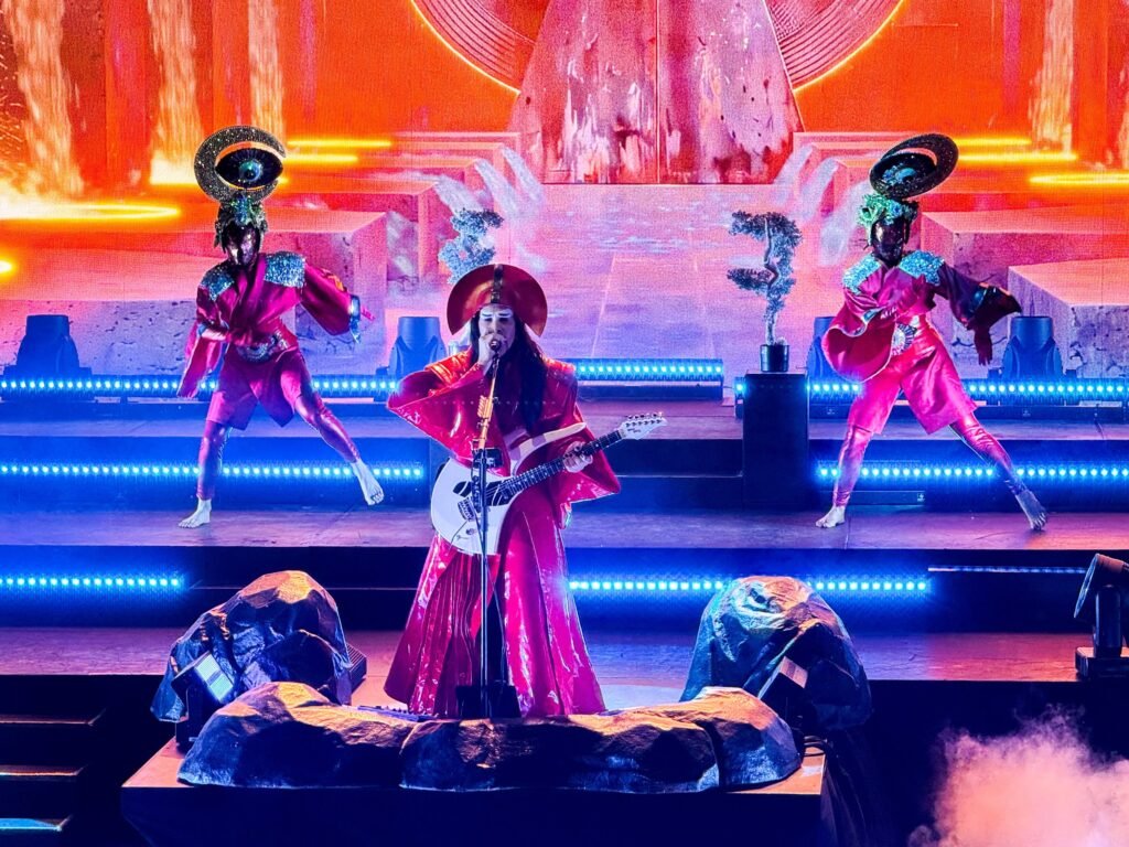 Erykah Badu performs live on a brightly lit stage, accompanied by dancers in unique costumes.