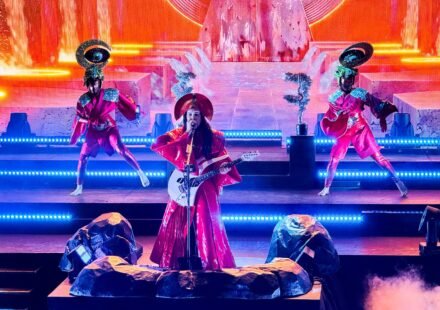 Erykah Badu performs live on a brightly lit stage, accompanied by dancers in unique costumes.
