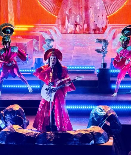 Erykah Badu performs live on a brightly lit stage, accompanied by dancers in unique costumes.