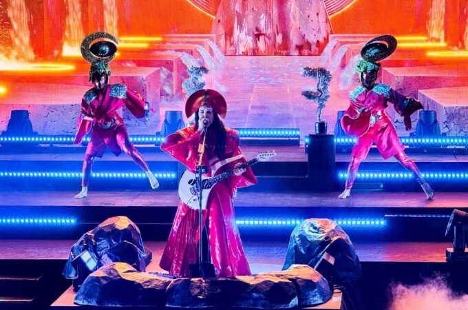 Erykah Badu performs live on a brightly lit stage, accompanied by dancers in unique costumes.