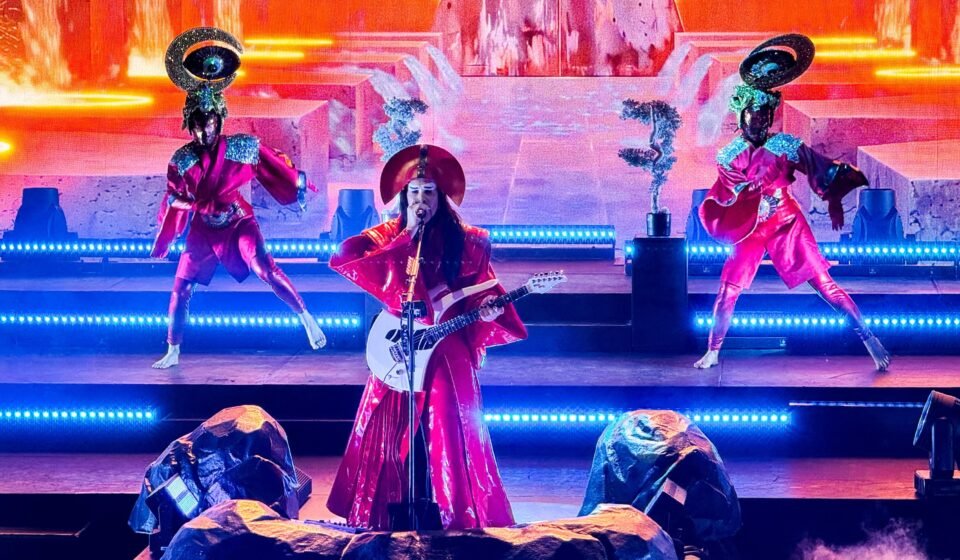 Erykah Badu performs live on a brightly lit stage, accompanied by dancers in unique costumes.