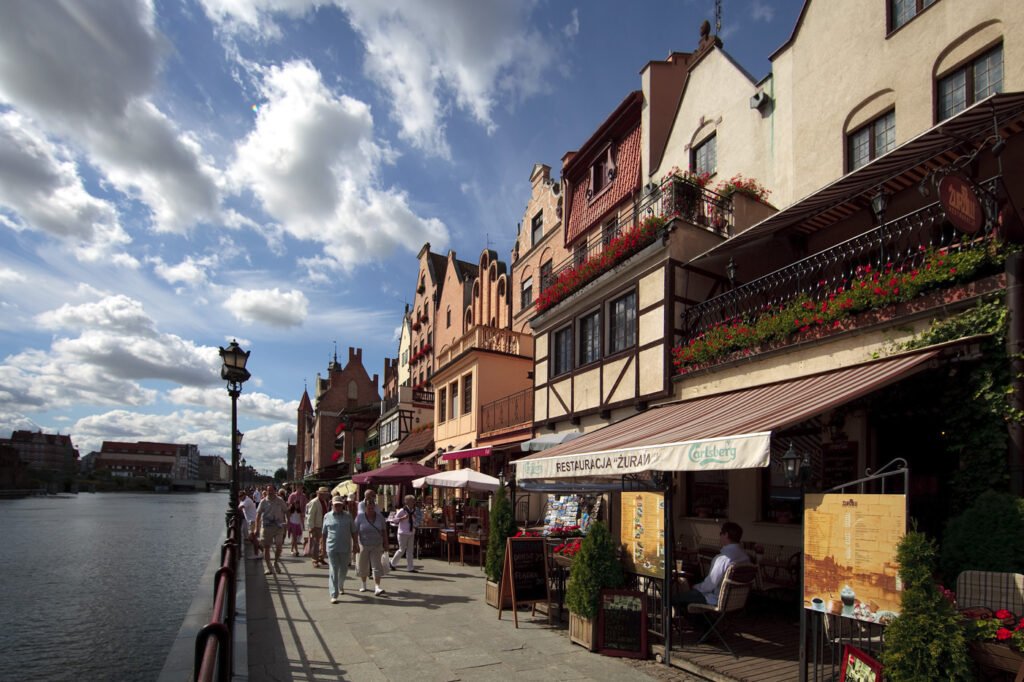A picturesque scene of a riverside promenade lined with quaint cafes and historical buildings under a bright sky.