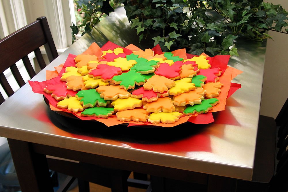 A tray filled with vibrant, fall-colored leaf-shaped cookies on a dining table.