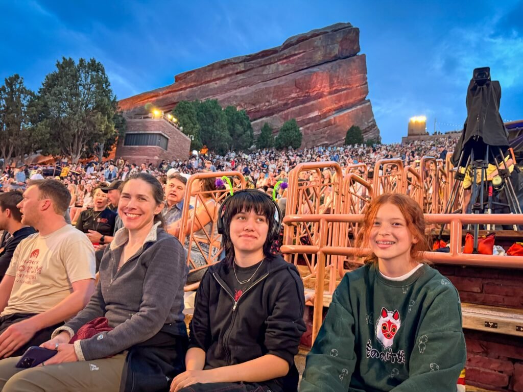 A family of four sitting together at a concert venue, with the iconic red rock formations in the background.