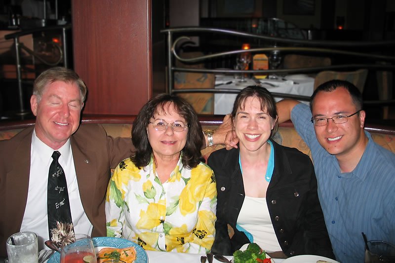 Four people smiling together at a dinner table. The setting appears to be a cozy restaurant.
