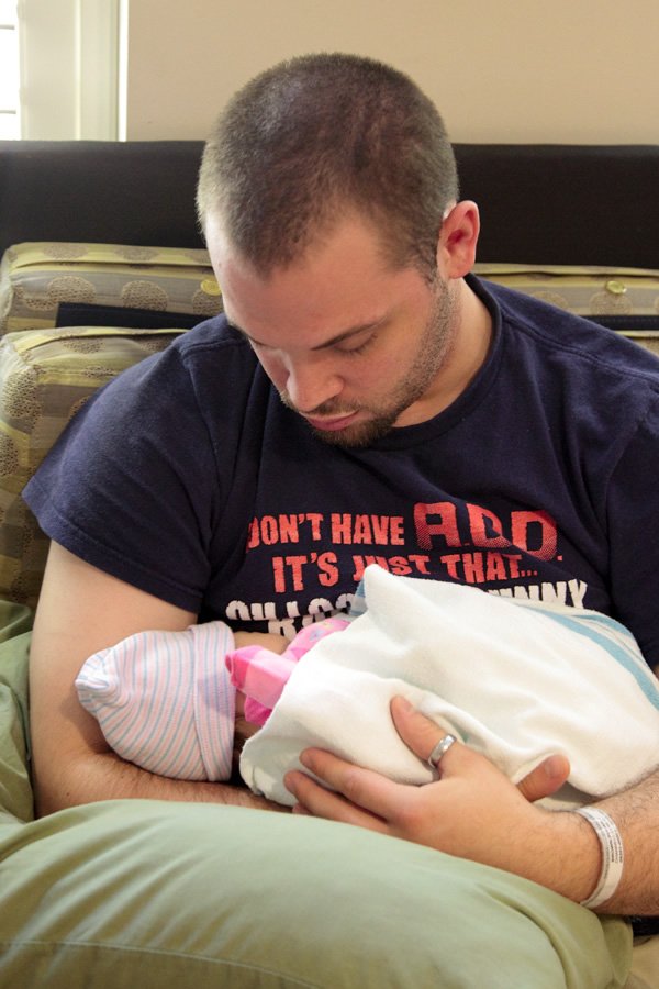 A moment of fatherly love shared with a newborn baby; baby hat and blankets in use.