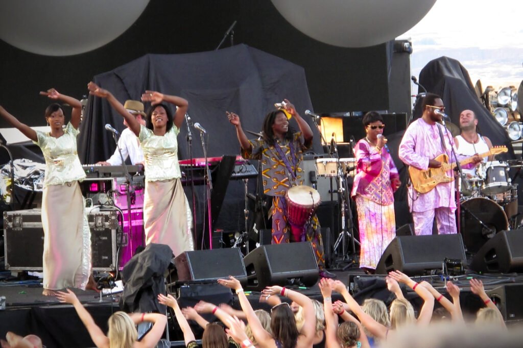 A vibrant festival stage features performers in colorful attire, engaging with an enthusiastic crowd.