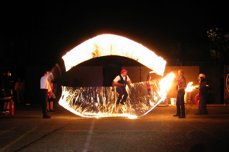 A fire dancer performs under the night sky, creating a glowing arch of flames.