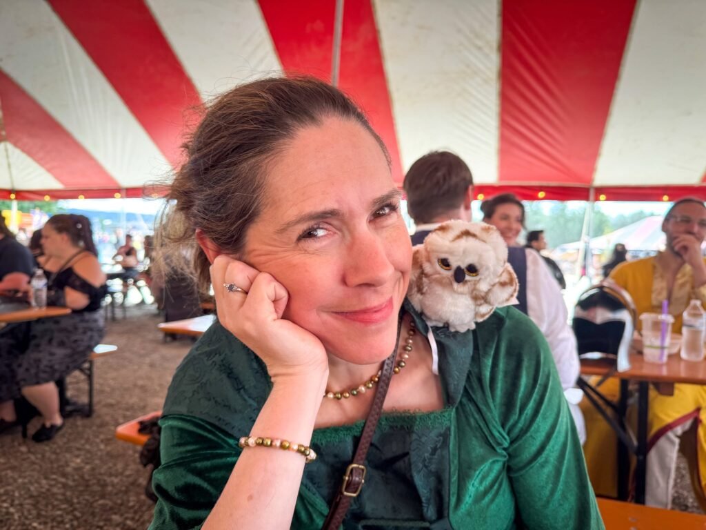 Kristie rests her head on her hand, smiling while holding a small dog under a red and white striped tent.