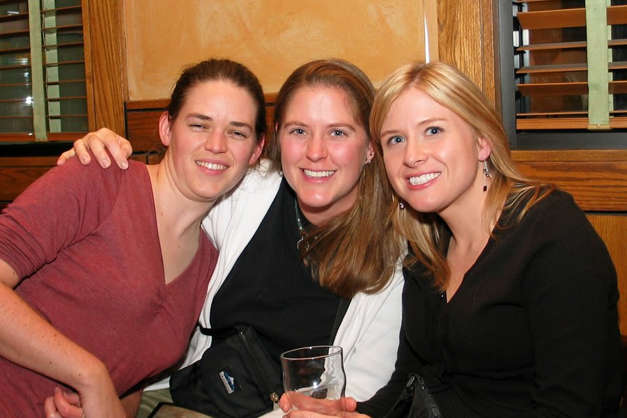 A photo of three women sitting together at a restaurant, smiling and enjoying drinks.