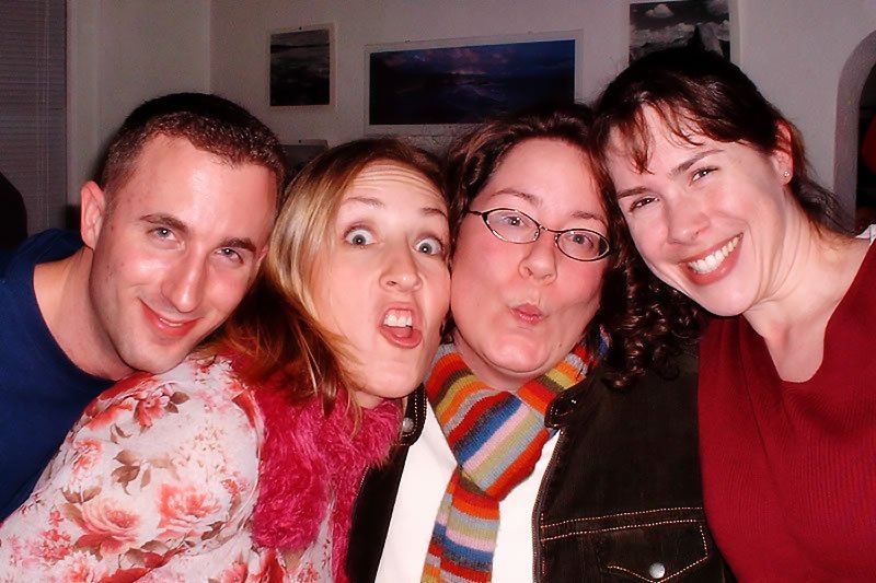 A group of four friends making playful faces and smiling for a casual indoor photo.