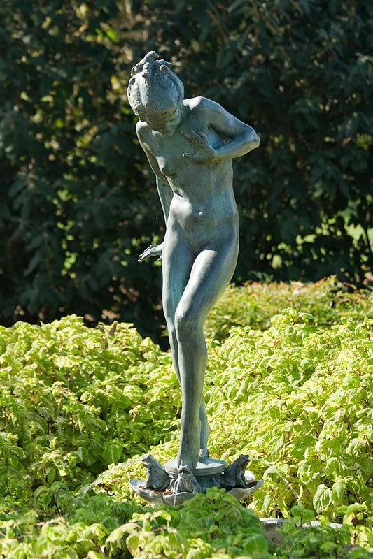 A serene garden scene featuring a statue of a person standing on a base with birds, set against lush and vibrant greenery.