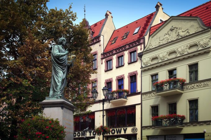 A serene statue surrounded by vibrant autumn foliage with charming old buildings in the background.