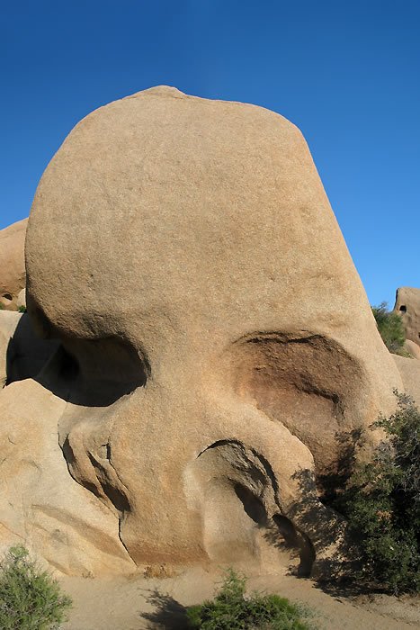 A large tan rock formation resembling a face under clear blue skies.