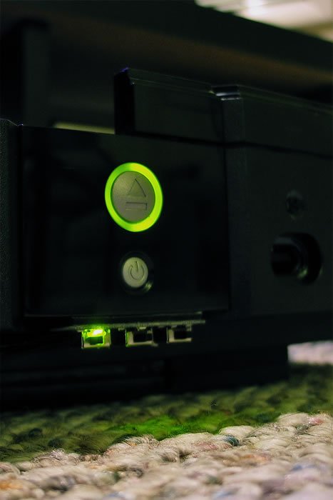 A close-up of a black device with a glowing green light, placed on a textured surface resembling moss or grass.